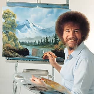 Bob Ross peint un paysage de montagne avec une barbe et tient un pinceau.