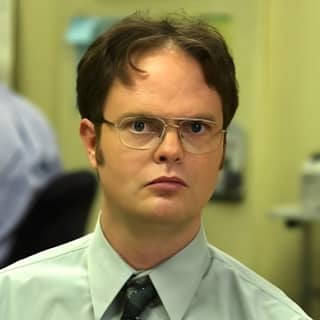 Dwight Schrute mengenakan kacamata dan dasi di kantor.