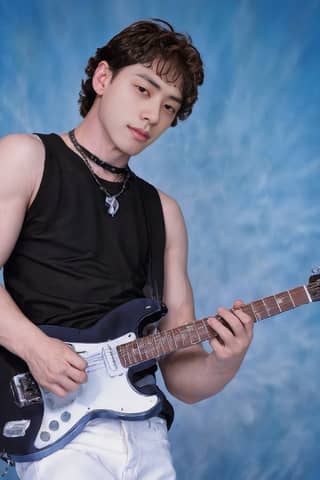 Man in black shirt playing guitar in front of blue background.