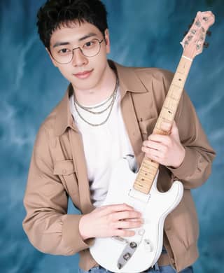 Man in glasses poses with a white guitar in front of a blue background.