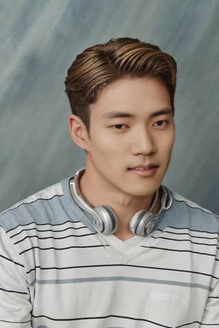 Man sitting in front of a blue wall wearing headphones and a striped shirt.