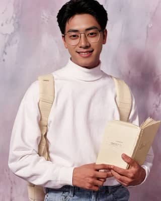 Homme souriant tout en tenant un livre et en portant des lunettes et des accessoires.