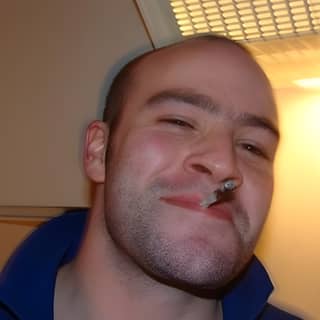 Homme souriant avec une cigarette dans la bouche.