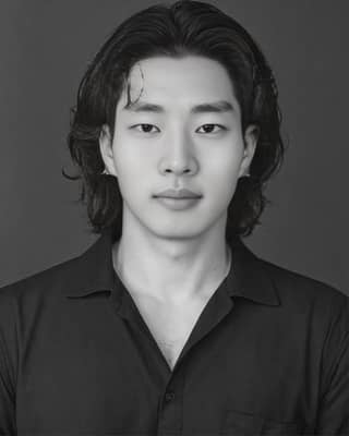 The actor is known for his role in the Korean drama 'The man who knew too much', with long black hair and wearing a black shirt.