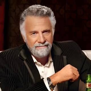 The most interesting man in the world sitting at a table with a beer.