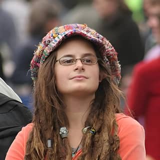 Woman with dreadlocks and glasses sits in a crowded street.