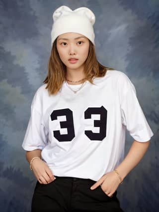 Femme portant un chemisier blanc avec le numero 33 dessus et un chapeau blanc posant pour une photo.