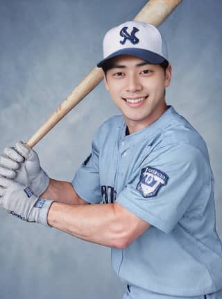 A baseball player in a blue uniform poses for a photo while holding a bat.