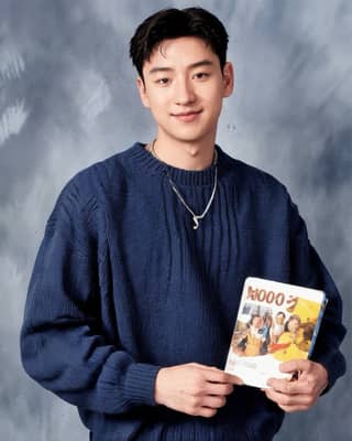 hombre con un suéter azul sosteniendo un libro con una imagen de un niño frente a un fondo gris.