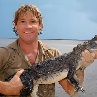 Un hombre sosteniendo un gran cocodrilo en el agua.