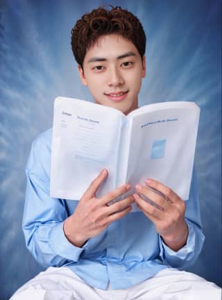 Um homem está sentado em uma cadeira, segurando um livro e sorrindo. Ele é um estudante em uma série de drama coreana.