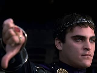 A man in a purple shirt and black pants holds a sword in a roman outfit.