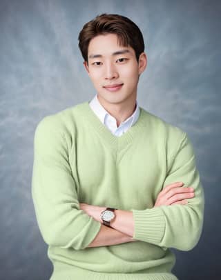 A man wearing a green sweater and white shirt is smiling.