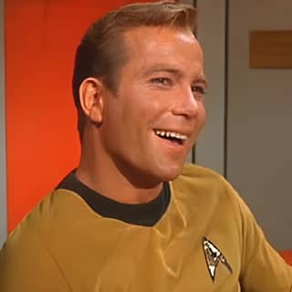 Um homem com uma camisa amarela sorri enquanto está sentado em uma cena do filme Star Trek.