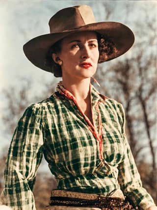 Una donna indossa una camicia a quadri verde e bianca e un cappello da cowboy sta cavalcando un cavallo.