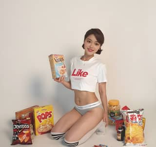 Woman in underwear holding a bag of chips and other snacks, sitting on the floor with a box of cereal. She is a model and actress.