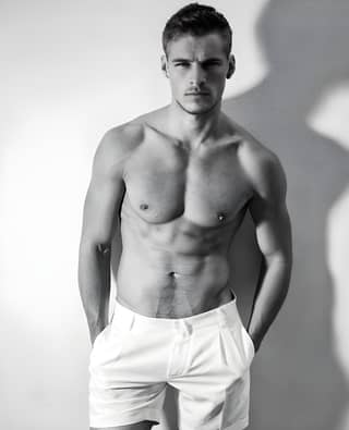 A shirtless man posing for a photo in white shorts.