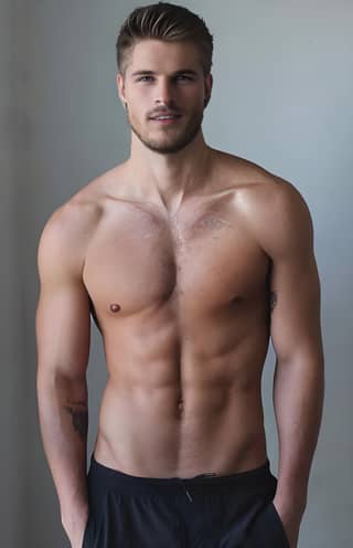 A shirtless man standing in front of a wall, posing.