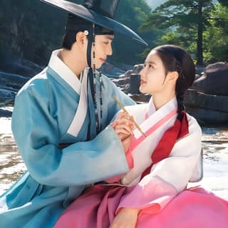 Asian couple in traditional Korean clothing sitting on a rock by the river.