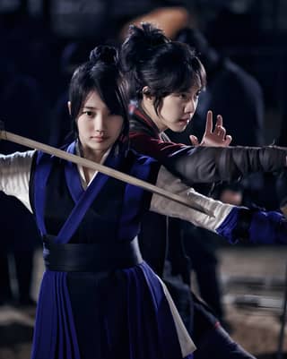 Two Asian women in traditional clothing holding swords, depicting a scene of strength and traditional culture.