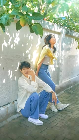 Two people sitting on the ground next to an orange tree and a wall. The girl fell in love with the boy repeatedly.