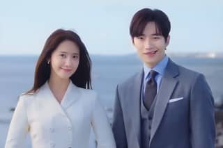 Two people in suits standing near the ocean.