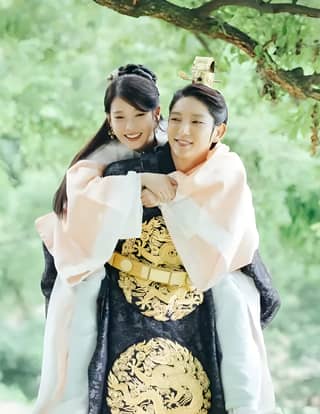 Two people in traditional clothing are posing for a photo, the bride and groom in the park.