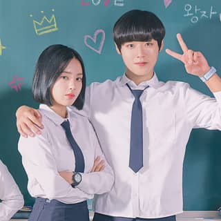 Two young people in school uniforms standing next to a chalkboard, posing for a picture.