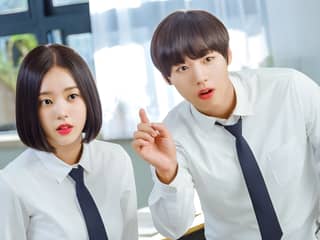 Two young people in white shirts and ties are in a room with a window and a desk.