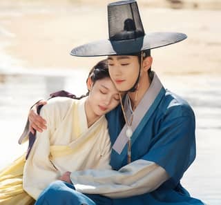 Woman in traditional hanbok on the beach, wearing a blue dress and hat.