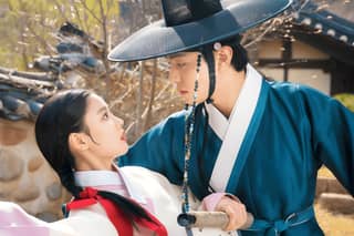 Woman wearing traditional Korean clothing, in a blue dress and black hat, featured in The King's Avatar drama.