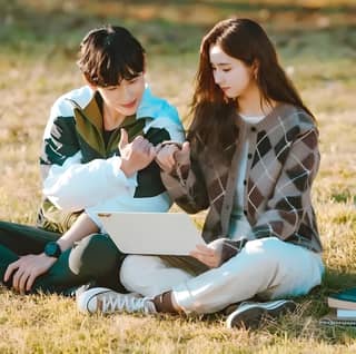 A couple are sitting on the grass and looking at a laptop.