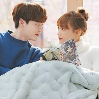 영화 'The Girl Next Door' 장면에서 여자가 이불을 덮고 소파에 앉아 있음