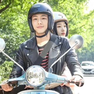 A woman rides a scooter with helmets on.