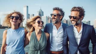 Cuatro personas en trajes y gafas de sol en un barco, dos parejas de hombres de 40 años ricos, sonrientes y saludables, y una mujer, felices juntos y bromeando, con un código de vestimenta de polo o smart casual, y algunos llevando gafas de sol caras y relojes.