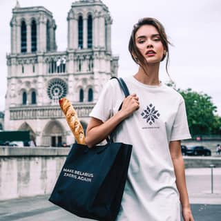 in a white dress and black bag holding a bag of bread