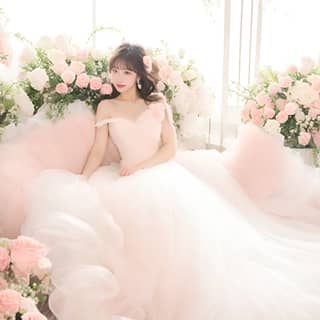 in a pink wedding dress sitting on a bed surrounded by pink flowers