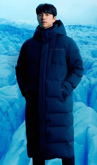 in a blue puffer coat standing in front of a glacier