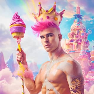 Una figura con cabello rosa y una corona está parada frente a un castillo de dulces.