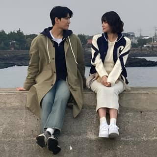 two people sitting on a wall near the ocean